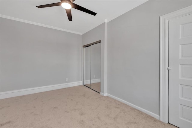 unfurnished bedroom with baseboards, light colored carpet, ceiling fan, ornamental molding, and a closet