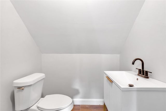 half bath featuring lofted ceiling, baseboards, vanity, and toilet