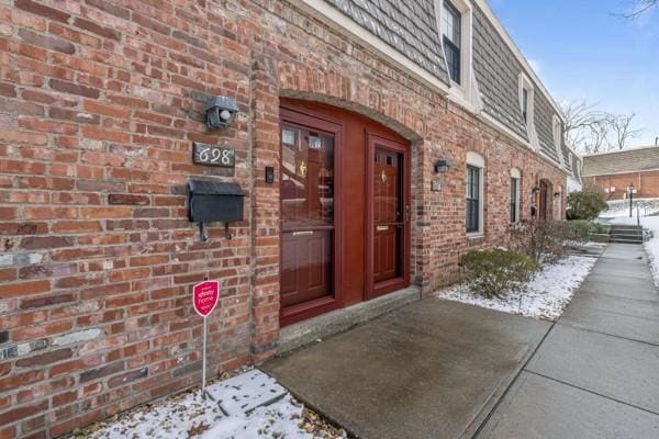 snow covered property entrance featuring brick siding and mansard roof