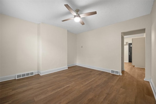 spare room with dark wood-style floors, visible vents, ceiling fan, and baseboards