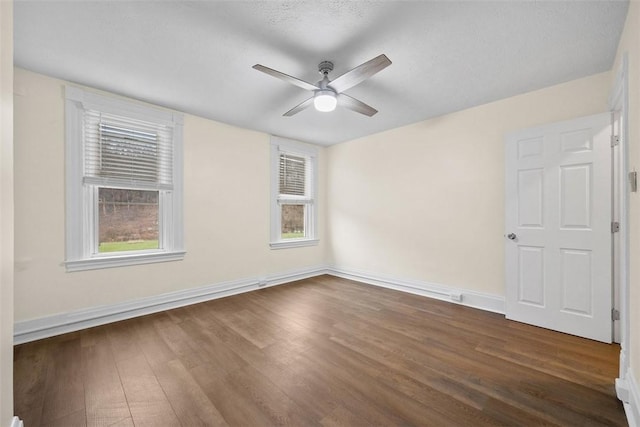 unfurnished room with a ceiling fan, a wealth of natural light, dark wood finished floors, and baseboards