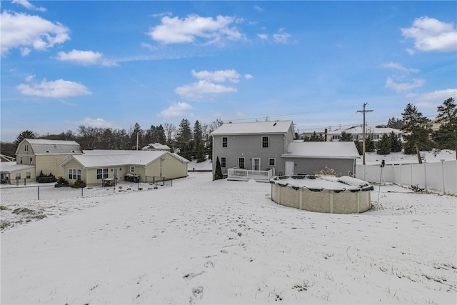 snow covered rear of property featuring a garage and fence