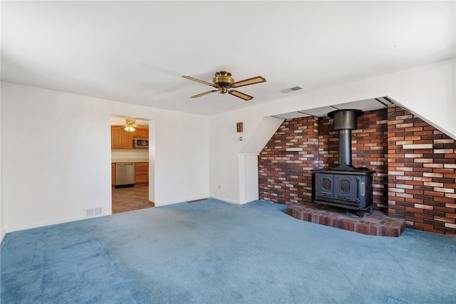 unfurnished living room with a wood stove, visible vents, ceiling fan, and carpet flooring