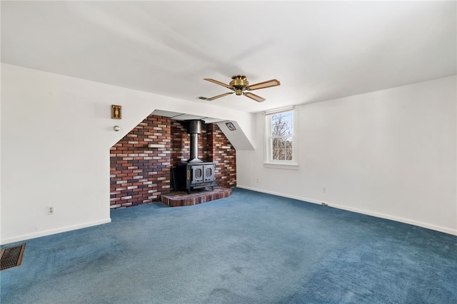 unfurnished living room featuring visible vents, baseboards, ceiling fan, a wood stove, and carpet