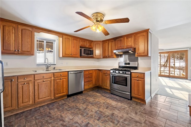 kitchen featuring under cabinet range hood, a sink, light countertops, appliances with stainless steel finishes, and brown cabinets