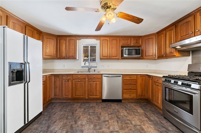 kitchen with under cabinet range hood, a sink, light countertops, appliances with stainless steel finishes, and brown cabinetry