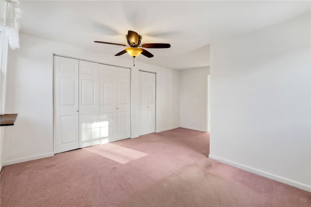 unfurnished bedroom with a ceiling fan, light colored carpet, baseboards, and multiple closets