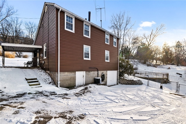 snow covered property featuring a garage, fence, a carport, and central air condition unit