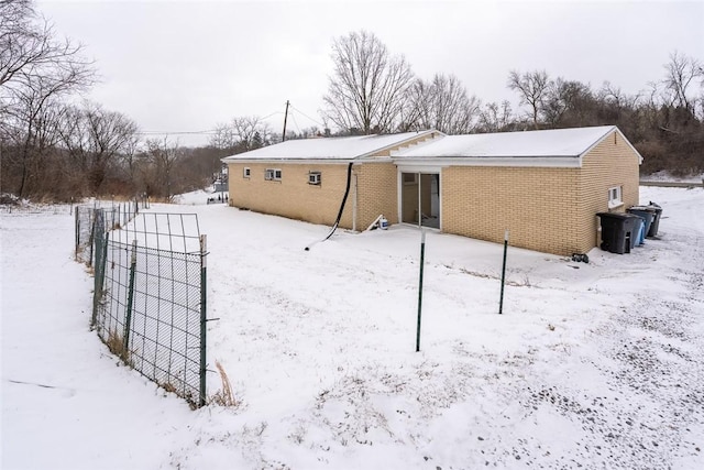 snow covered rear of property with brick siding and fence