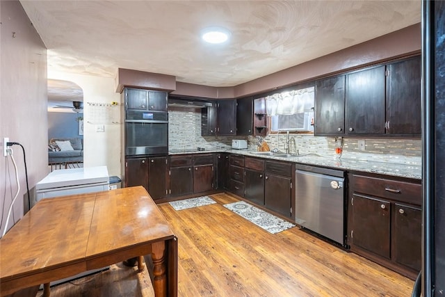 kitchen with stainless steel dishwasher, wall oven, dark brown cabinetry, and light wood-style floors