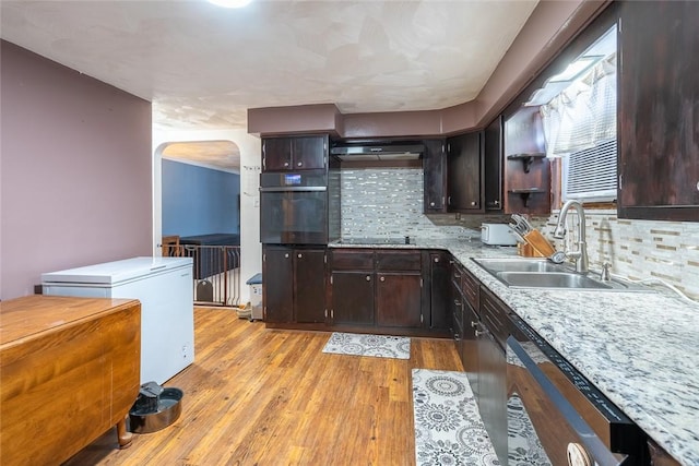 kitchen with arched walkways, light countertops, a sink, light wood-type flooring, and black appliances