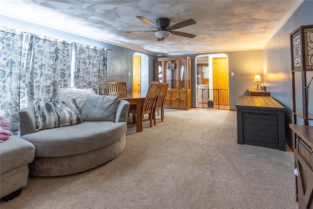 living area with a ceiling fan, arched walkways, crown molding, and light colored carpet