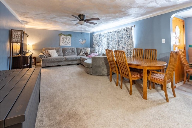 dining area featuring light carpet, ceiling fan, and arched walkways