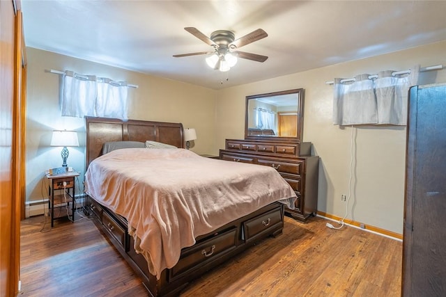 bedroom with dark wood-style floors, ceiling fan, baseboards, and a baseboard heating unit