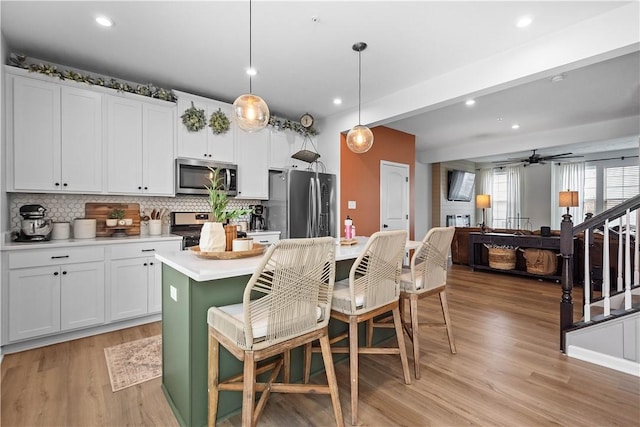 kitchen with an island with sink, decorative light fixtures, stainless steel appliances, light countertops, and white cabinetry