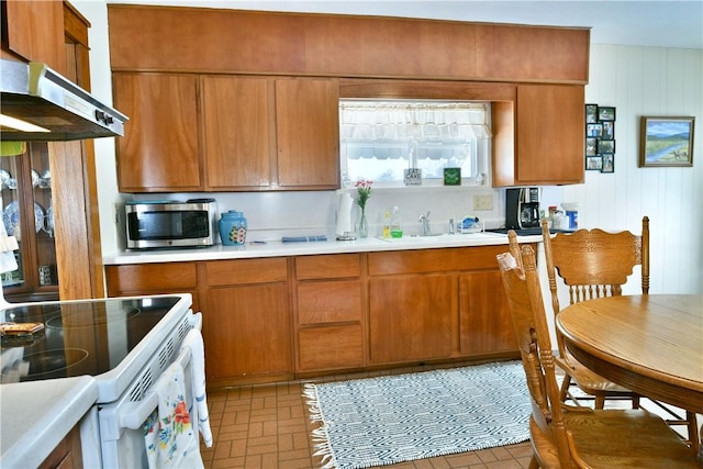 kitchen featuring white electric stove, brown cabinetry, stainless steel microwave, light countertops, and a sink