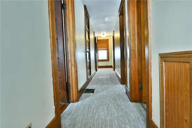 hallway featuring light carpet, visible vents, and baseboards