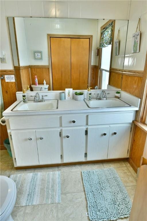 bathroom featuring double vanity, wooden walls, a sink, and wainscoting