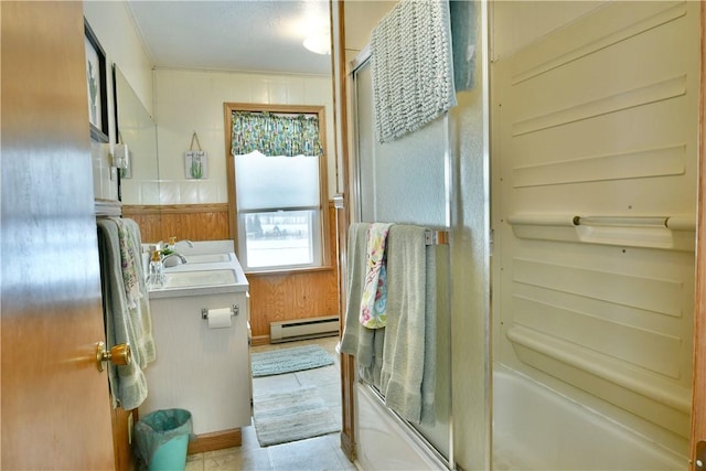 bathroom with double vanity, a baseboard radiator, combined bath / shower with glass door, a sink, and wooden walls