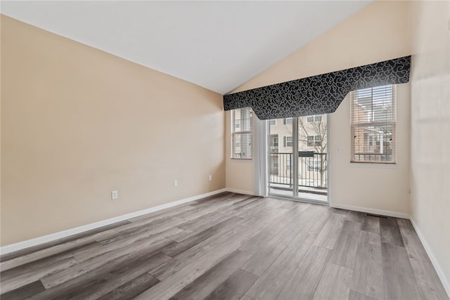 spare room with lofted ceiling, baseboards, and light wood-style floors