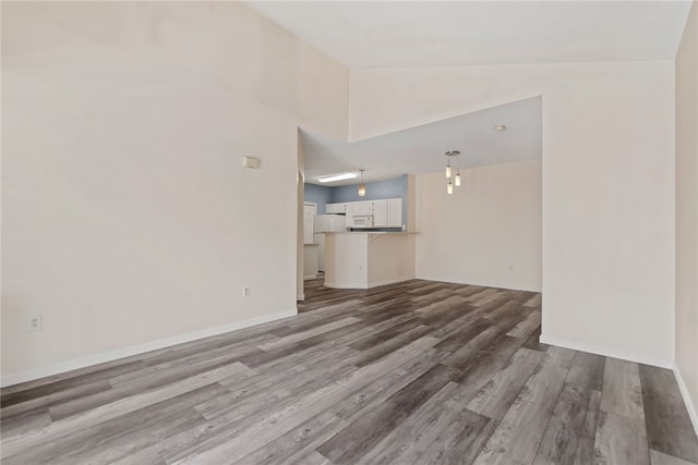 unfurnished living room featuring lofted ceiling, baseboards, and wood finished floors