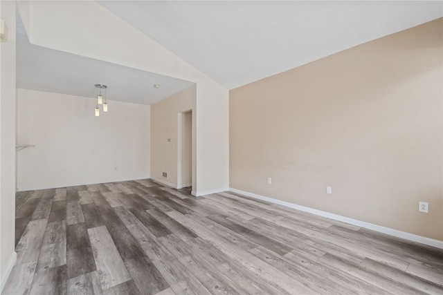 spare room with light wood-type flooring, baseboards, and vaulted ceiling