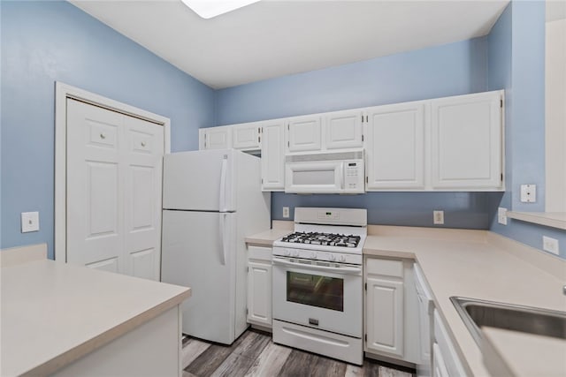 kitchen with light countertops, white cabinetry, a sink, wood finished floors, and white appliances