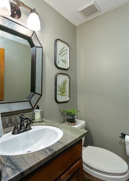 half bathroom featuring toilet, vanity, and visible vents