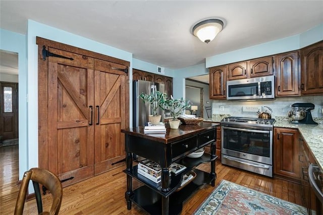 kitchen with a barn door, decorative backsplash, light stone counters, stainless steel appliances, and light wood-style floors