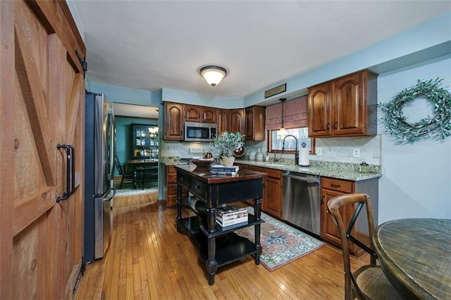 kitchen with light wood-style flooring, stainless steel appliances, a sink, backsplash, and brown cabinets