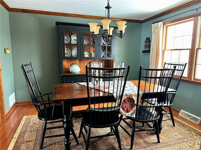 dining area with ornamental molding, wood finished floors, visible vents, and an inviting chandelier