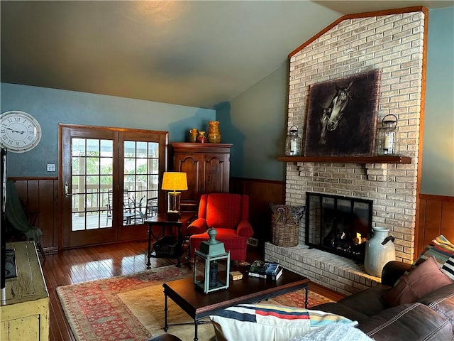 living area featuring a wainscoted wall, wood walls, vaulted ceiling, a brick fireplace, and hardwood / wood-style floors