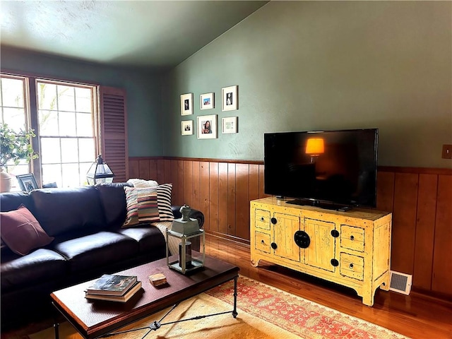 living room featuring wainscoting, wood finished floors, visible vents, and wooden walls