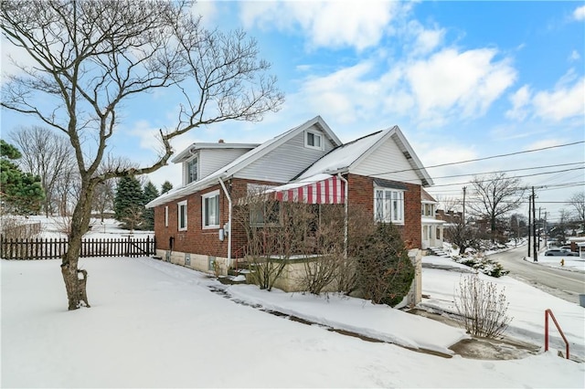 view of snow covered exterior featuring brick siding and fence