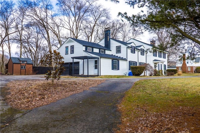 view of front of home with a chimney, aphalt driveway, an outbuilding, a shed, and a front lawn