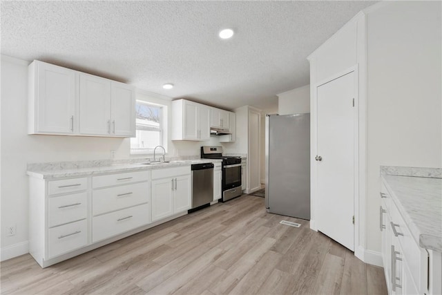 kitchen featuring a textured ceiling, stainless steel appliances, light wood finished floors, and white cabinetry