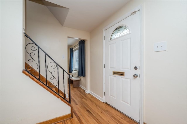 foyer entrance featuring light wood-style flooring, stairway, and baseboards