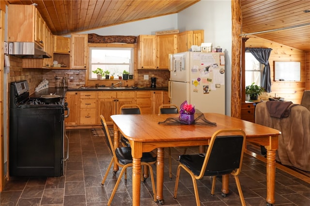 kitchen featuring under cabinet range hood, vaulted ceiling, freestanding refrigerator, dark countertops, and range with gas cooktop