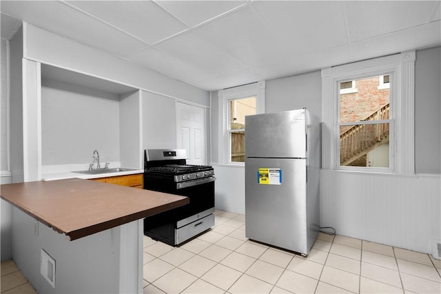 kitchen with light tile patterned floors, a peninsula, stainless steel appliances, a kitchen bar, and a sink