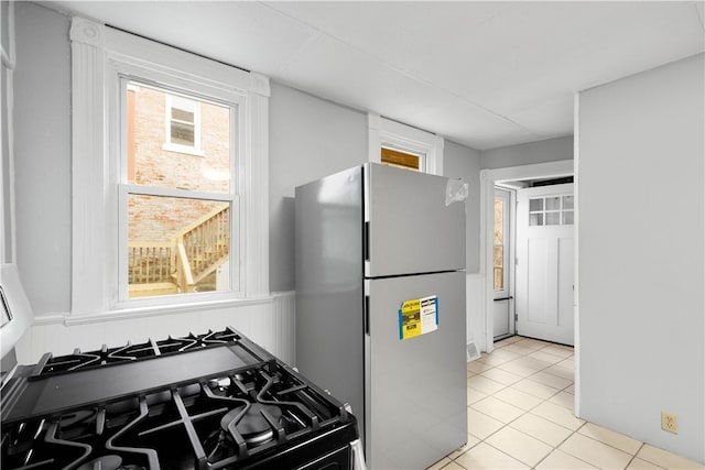 kitchen featuring a healthy amount of sunlight, light tile patterned floors, gas range oven, and freestanding refrigerator