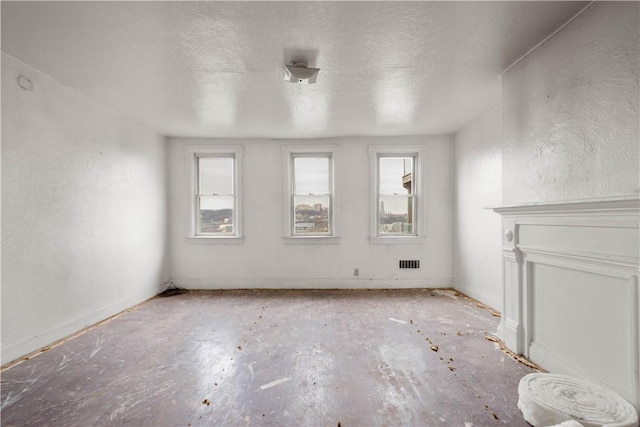 unfurnished living room featuring a textured ceiling, a textured wall, visible vents, and a wealth of natural light