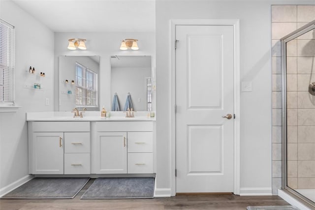 full bath featuring a sink, wood finished floors, baseboards, a shower stall, and double vanity