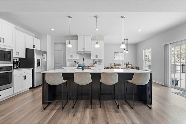 kitchen featuring appliances with stainless steel finishes, light countertops, decorative light fixtures, and an island with sink