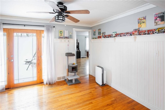 empty room featuring wainscoting, visible vents, crown molding, and wood finished floors