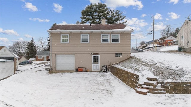 snow covered back of property with a garage, a chimney, and cooling unit