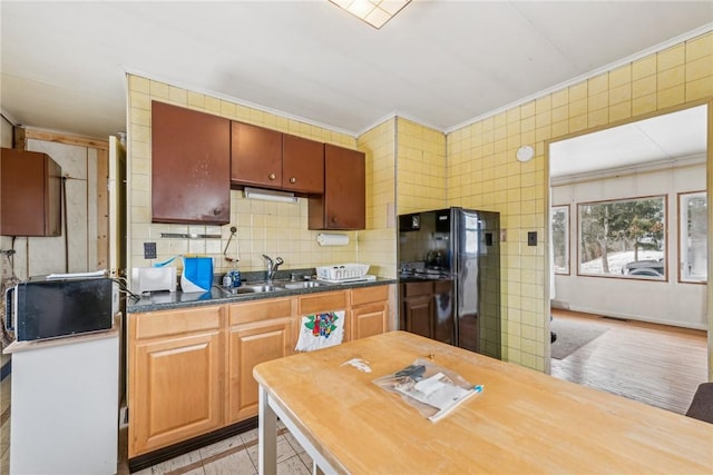 kitchen featuring visible vents, brown cabinetry, ornamental molding, freestanding refrigerator, and a sink