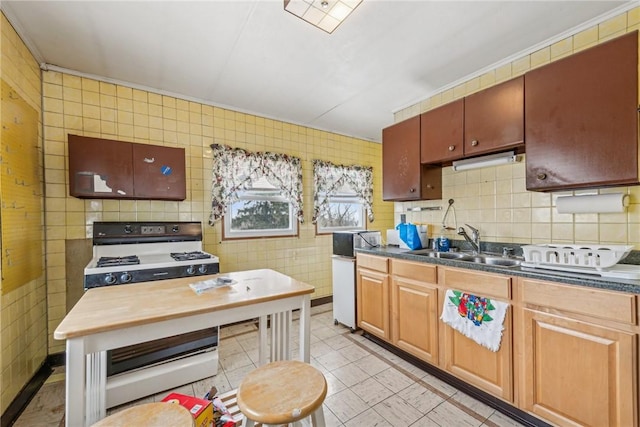 kitchen featuring range with gas cooktop, brown cabinets, tile walls, dark countertops, and a sink