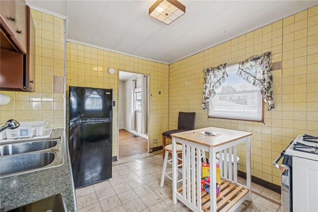 kitchen with white range with gas stovetop, a sink, tile walls, freestanding refrigerator, and crown molding