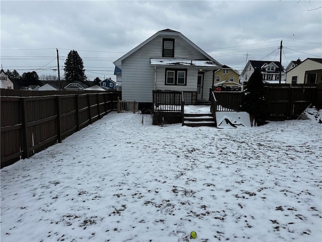 snow covered rear of property with a deck, fence, and a residential view