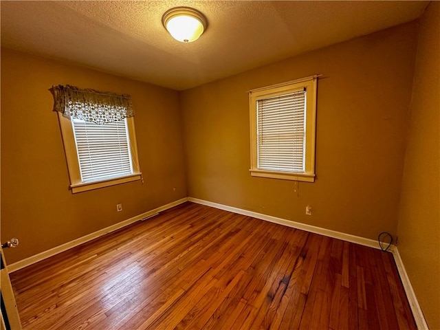 empty room with a textured ceiling, wood finished floors, and baseboards